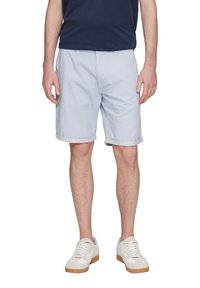 Hellblaue Baumwollshorts mit umgeschlagenen Säumen, seitlichen Taschen und flachem Frontdesign. Kombiniert mit weißen Sneakers mit Gummisohlen.
