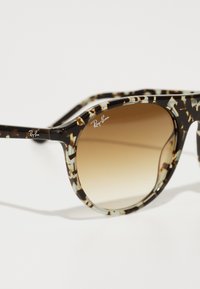 Ochelari de soare Ray-Ban cu un cadru din plastic cu un model maro și negru, lentile maro cu gradient și accente argintii cu logo pe templu.