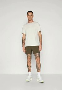 Camiseta de algodón blanca, pantalones cortos verdes oliva, calzado deportivo con acentos en blanco y verde claro, presentado sobre un fondo liso.