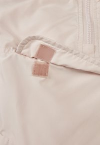 Šviesiai rožinė medžiaga su lygiu paviršiumi turi užtrauktuką ir dvi Velcro juosteles. Dizainas turi sulenktą kraštą, kad atrodytų tvarkingai.