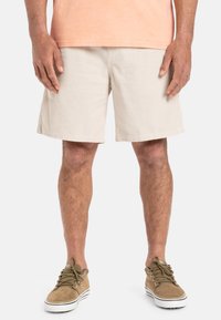 Pantalones cortos de pana beige con un corte recto, que cuentan con dos bolsillos laterales y una textura suave, combinados con zapatos de cordones color marrón claro.