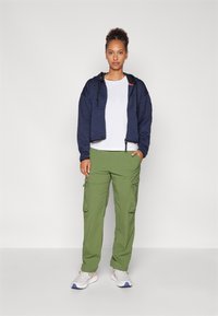 Marineblå kort sweatshirt med teksturert stoff, parret med lysegrønne cargo-bukser med sidelommer. Hvit t-skjorte og grå joggesko fullfører stilen.