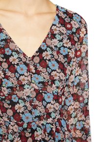 Vestido floral com decote em V, apresentando um fundo preto e um padrão de flores azuis, vermelhas e rosas; tecido leve e transparente.