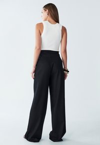 Bela rebrasta majica na brez rokavih, v kombinaciji z črnimi hlačami širokih hlačnic. Hlače imajo gladko teksturo in visok pas.