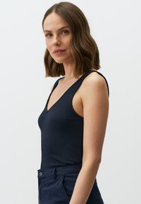 Top in cotone a coste di colore blu navy con scollatura a V profonda e spalline spesse, abbinato a pantaloni scuri a vita alta che mettono in mostra una texture liscia.