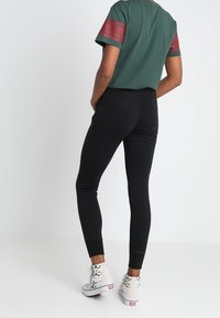 Grön t-shirt med röda randiga ärmar, svarta slim-fit byxor och mönstrade sneakers, med fokus på färger och design detaljer.