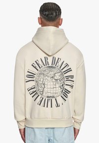 Felpa color crema con una grande grafica di un globo e testo sul retro. Presenta un cappuccio con coulisse e polsini a costine sulle maniche e sull'orlo.