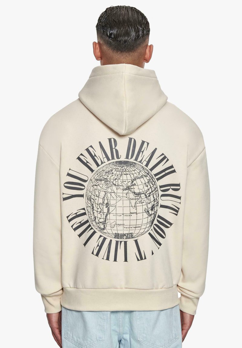 Felpa color crema con una grande grafica di un globo e testo sul retro. Presenta un cappuccio con coulisse e polsini a costine sulle maniche e sull'orlo.