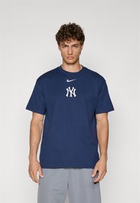Námornícky bavlnený tričko s krátkymi rukávmi a okrúhlym výstrihom. Obsahuje biele vyšívané logo New York Yankees a malý Nike swoosh nad ním.