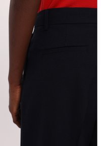 Pantaloni su misura blu navy con texture liscia, dotati di una singola tasca posteriore e design slim fit. Dettagli visibili sulla vita.