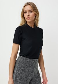 Top fitted nero a maniche corte con scollo rotondo, realizzato in un tessuto liscio. Il modello indossa pantaloni high-waisted grigi a motivo houndstooth.