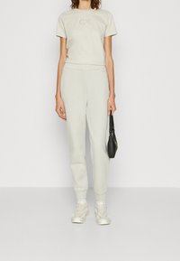 T-shirt in cotone grigio chiaro con un logo sottile, abbinato a pantaloni della tuta coordinati. Tessuto texturizzato, vestibilità comoda e sneakers bianche completano l'outfit.