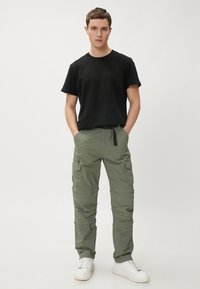 Zwart T-shirt met korte mouwen, gecombineerd met olijfgroene cargo broek. De broek heeft meerdere zakken en een koord in de taille. Witte sneakers.