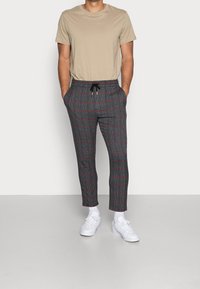Pantaloni grigi a quadri con accenti rossi, dotati di una comoda vita elastica e stringa, abbinati a una t-shirt beige e sneakers bianche.