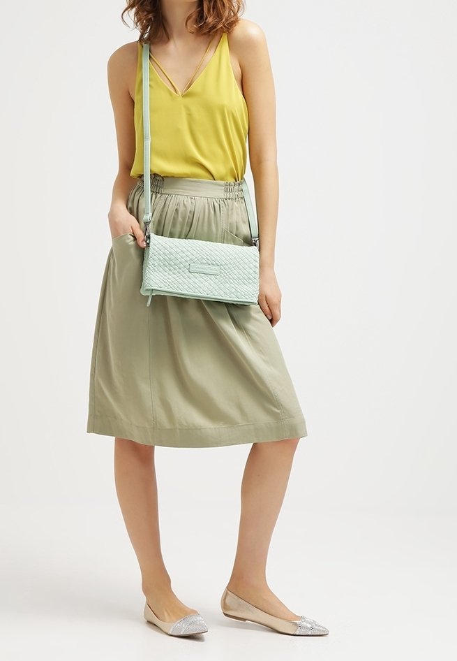 Sac à bandoulière tissé menthe avec une texture lisse, porté avec un débardeur jaune et une jupe vert clair, associé à des ballerines argentées.