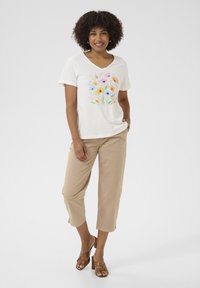 Cream V-neck T-shirt featuring a colorful floral print, paired with beige cropped pants and brown block-heeled sandals.