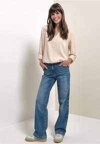 Lys beige skjorte med lange ærmer og en afslappet pasform, parret med brede blå jeans og cremede sneakers med blå accenter.