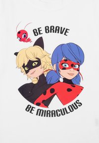 T-shirt bianco con personaggi dei cartoni animati dai capelli biondi e gli occhi verdi, e capelli blu con macchie rosse, circondati dal testo "SII CORAGGIOSO SII MIRACOLOSO."