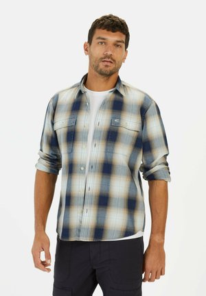 Geruite shirt in blauw, crème en bruine tinten; lange mouwen opgerold, twee knoopzakken op de borst en een knoopsluiting aan de voorkant. Katoenen stof.