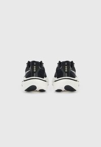 Ζευγάρι ασπρόμαυρα αθλητικά παπούτσια, φαίνονται από πίσω, με ύφασμα από δίχτυ, επενδυμένες σόλες και αντανακλαστικές λεπτομέρειες σε γκρίζο φόντο.