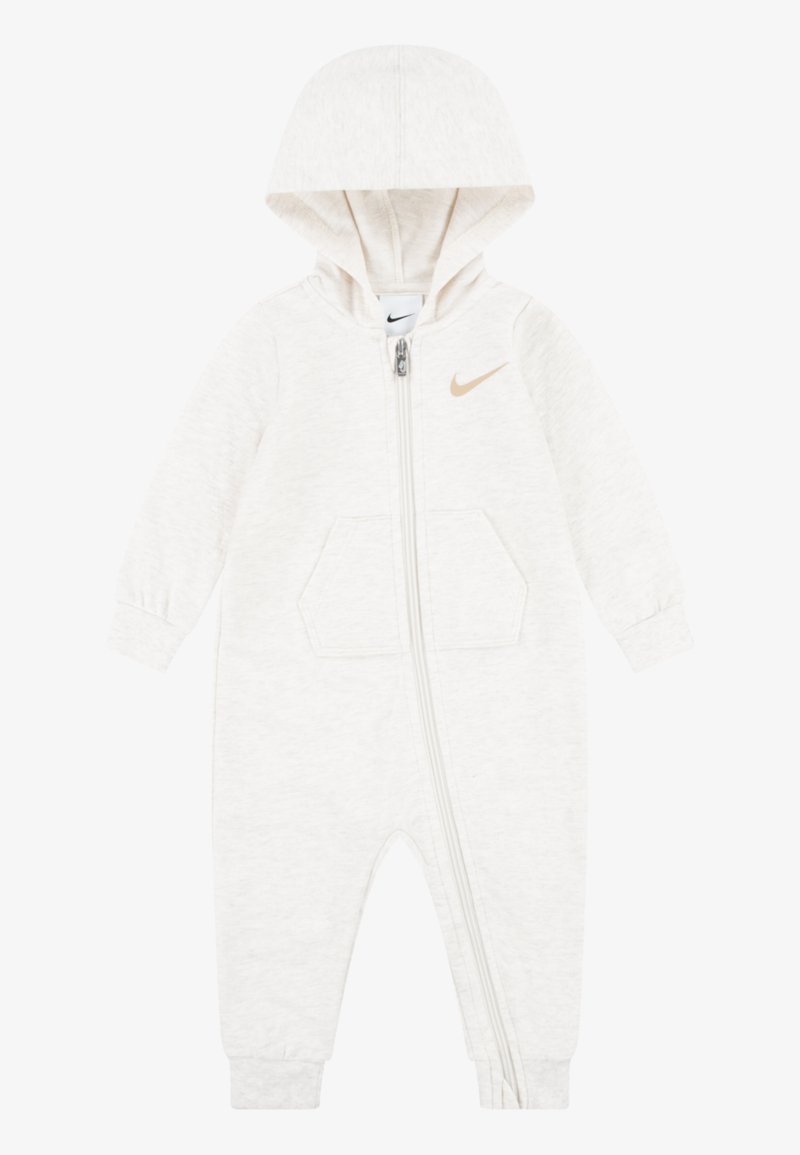 Light beige zip-up onesie with a hood, featuring a small gold Nike logo, front pockets, and ribbed cuffs. Soft fabric with a smooth texture.