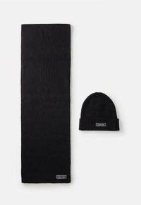Czarny żeberkowany szalik i pasująca czapka beanie, oba z białymi prostokątnymi naszywkami z logo Calvin Klein na białym tle.