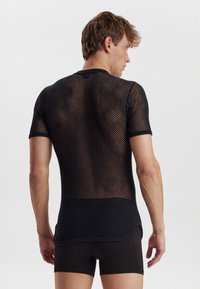 Sort mesh skjorte med korte ærmer og rund udskæring. Åben vævemønster med en buet kant, båret over sorte shorts.