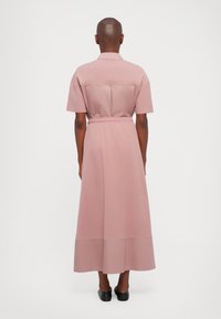Rosa midikjole med korte ermer, kragehals og belte i livet. Stoffet ser mykt ut med en jevn tekstur og minimale designdetaljer.