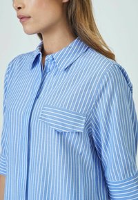 Light blue button-up shirt made of woven fabric, featuring vertical white stripes, a chest pocket, and short sleeves.
