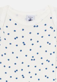 Hvit babydress med blått eplemønster og bølgete halslinning, størrelseetikett som viser 18 måneder/81 cm.