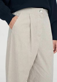 Helle beige gestreifte Hosen mit hoher Taille, Falten und seitlichen Taschen; ausgestattet mit einem einzelnen Metallknopf und einer glatten Textur.