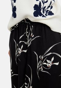 Schwarze Blumenhose mit weißem botanischem Muster und roten Akzenten. Hergestellt aus weichem Stoff mit elastischem Bund und Kordelzug.