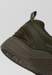 Olijfgroen sportschoen van mesh en textiel, met een gevoerde kraag, trekband en een geprofileerde rubberen zool voor grip.