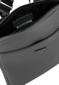 Graue Umhängetasche mit strukturiertem Finish, Reißverschluss und Logodetail. Das Innere ist mit einem logo-gedruckten Futter ausgestattet. Verstellbarer Schultergurt.