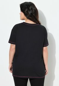 Camiseta de algodón negra con mangas cortas, dobladillo curvado y costuras en contraste en color rosa a lo largo del cuello y los bordes de las mangas.