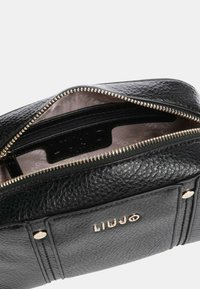 Czarna skóropodobna torba z teksturą, z elementami w kolorze złotym, wyposażona w zamknięcie na zamek oraz wewnętrzne przegródki, w tym metkę marki.