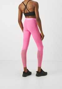 Tight rosa leggings med nätpaneler vid vaderna, parat med en svart sport-bh med korsade band och logotypdetalj.