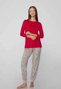Haut long rouge à manches longues associé à un pantalon de pyjama gris avec un imprimé de chien festif portant des chapeaux de Santa ; tissu doux et design ajusté.