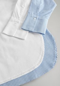 Camicia con bottoni caratterizzata da un collo bianco solido e un polsino a righe blu. Orlo arrotondato con tessuto a righe blu e bianche a contrasto.