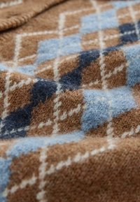 Närbild av mjukt ulltyg med ett rutigt mönster i bruna-, blå-, marinblå- och vita nyanser, som visar textur och vävdetaljer.