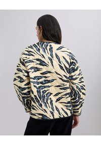Chaqueta acolchada en crema con rayas de tigre negras y azules. Cuenta con un cuello redondo y mangas largas, con un patrón de costura de diamante visible.