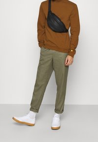 Brun sweatshirt, olivgrönt tapered byxor, vita sneakers med gummisula och en svart crossbody-väska. Slät tyg och avslappnad passform.