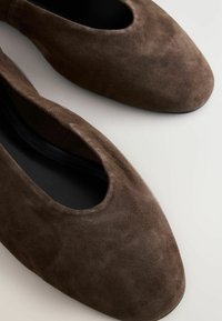 Zapatos planos de ante marrón con puntera redondeada y un corte en el lateral, exhibidos sobre un fondo claro.