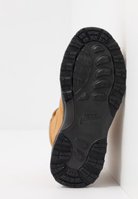 Obuv Nike s hnědým koženým svrškem, černou gumovou podrážkou s hlubokým vzorem a vyraženým logem na spodní části, navržená pro trakci.