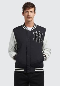 Zwart en lichtgrijs varsityjack met gestreepte ribgebreide kraag en manchetten, drukknoopsluiting en geborduurd logo op de borst.