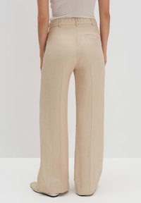 Pantalons larges beiges avec une texture lisse, une taille élastique et une poche arrière unique. Le tissu drape doucement, créant une silhouette fluide.
