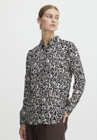 Long-sleeve button-up shirt in black and white abstract pattern, with a classic collar and two front pockets, made from lightweight fabric.
