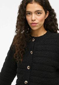 Zwarte textuur cardigan met een ronde hals, voorste knoopsluiting met lichtgekleurde knopen en een zachte, harige stof.
