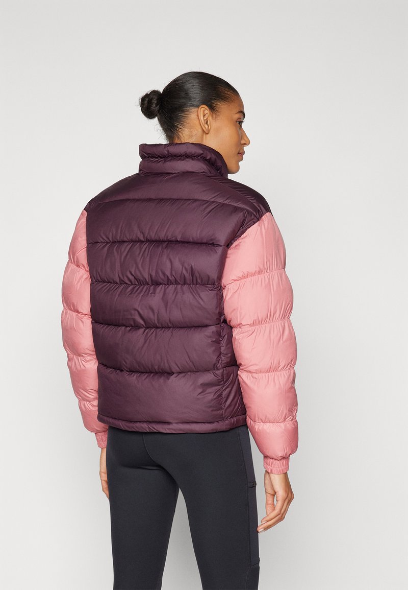 Giacca imbottita con un corpo viola e maniche rosa, colletto alto, polsini elasticizzati e tessuto trapuntato. Sotto indossa leggings neri.