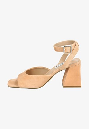 Nude semišové sandály na vysokém podpatku se čtveratou špičkou, otevřenými stranami a masivním, ostrým podpatkem. Obsahují nastavitelný pás na kotníku se sponou.